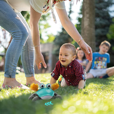 Enfant souriant poursuivant un jouet crabe interactif sur l'herbe, sous la surveillance d'un adulte, avec des enfants jouant en arrière-plan.