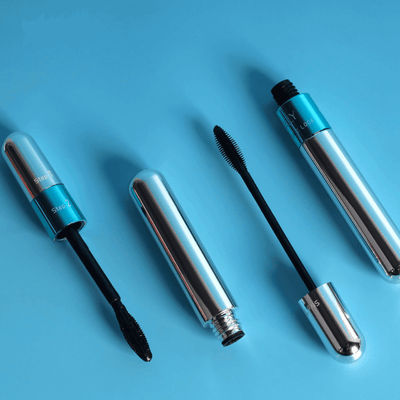 Quatre mascaras argentés et bleus sur fond bleu, ouverts et fermés, avec brosses noires. Maquillage yeux, cosmétique beauté, accessoires féminins.