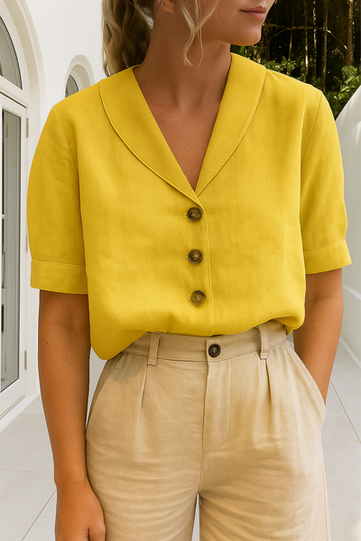 Femme portant une chemise jaune à col large et boutons marron, associée à un pantalon beige, devant une maison moderne. Mode estivale élégante.