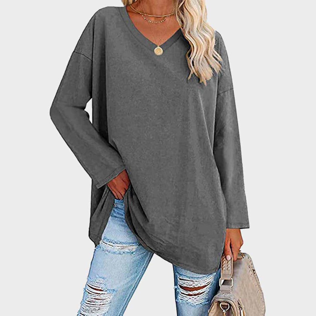 Femme portant un pull gris ample à col en V, associé à un jean déchiré et un sac beige. Mode décontractée, tendance automne-hiver.