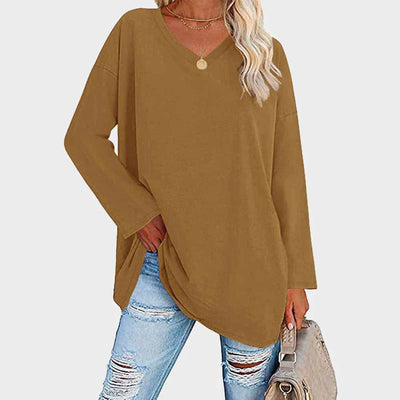 Femme portant un pull oversize marron à col en V, associé à un jean déchiré bleu clair et un sac beige. Mode décontractée automne-hiver.