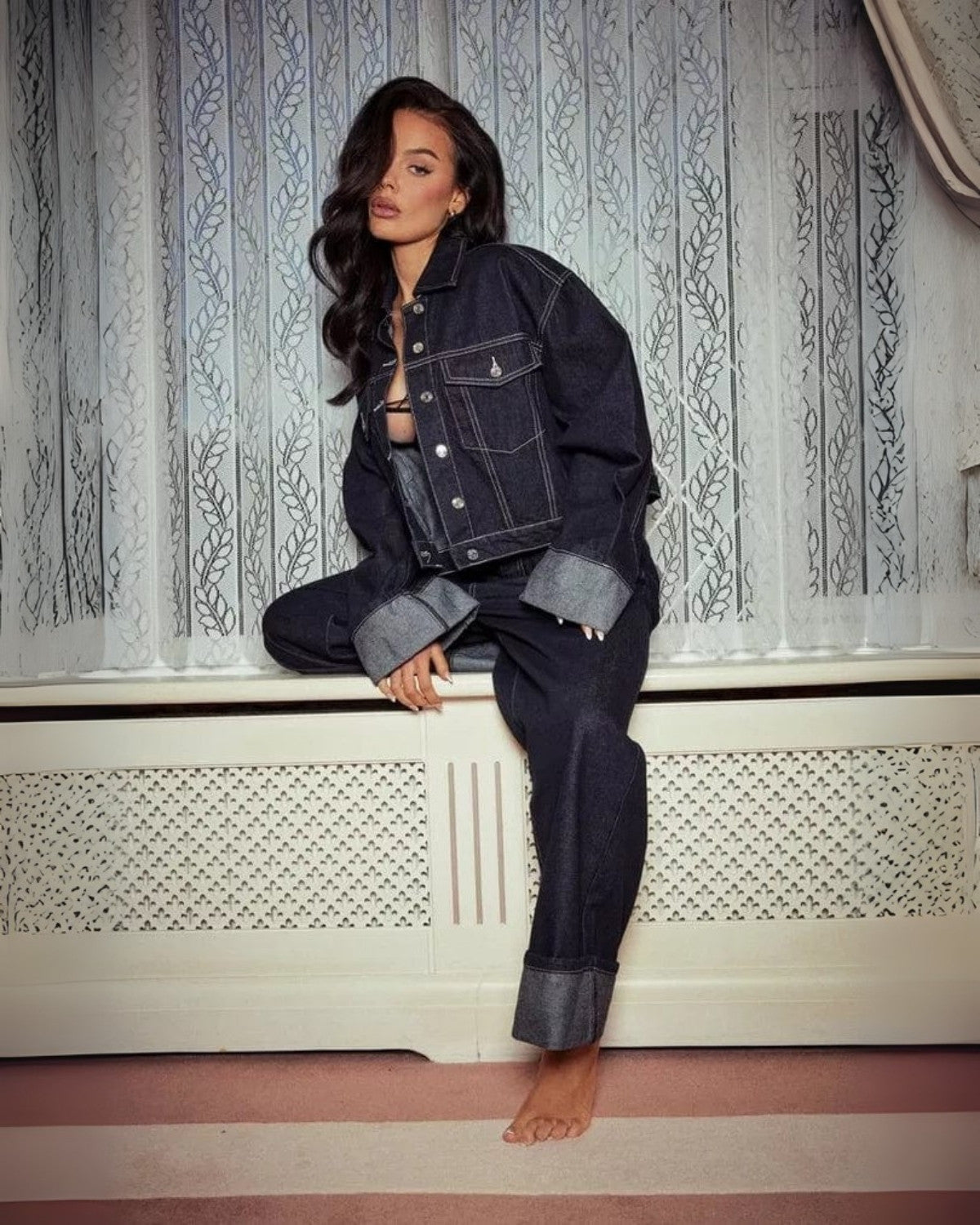 Jeune femme posant en tenue denim devant un rideau blanc, veste et pantalon en jean, ambiance décontractée et moderne, mode urbaine tendance.