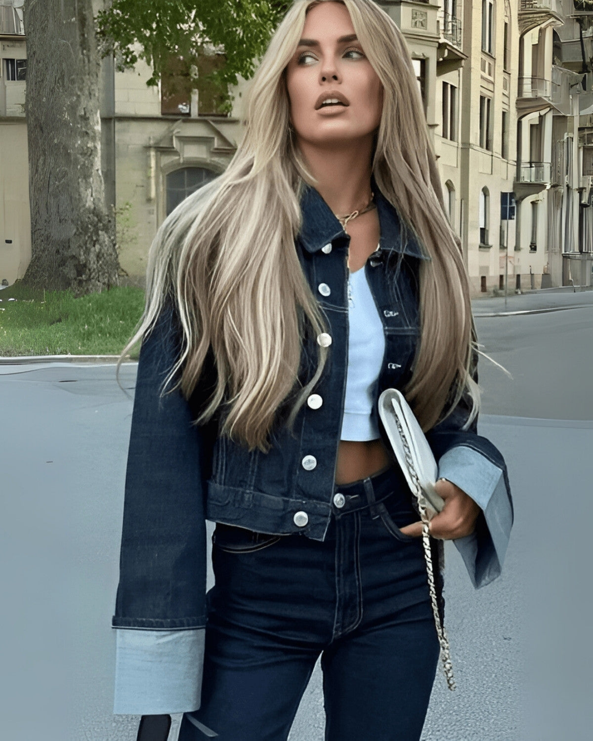 Jeune femme blonde en veste en jean et pantalon assorti, marchant en ville. Mode urbaine, style décontracté, cheveux longs, sac à main blanc.