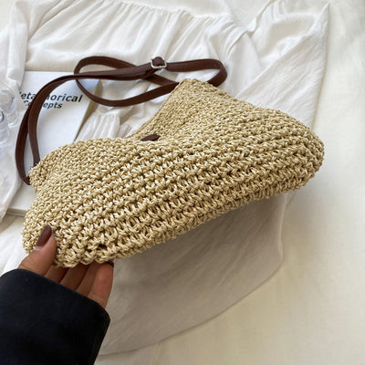 Sac en paille tressée beige avec bandoulière marron, posé sur une chemise blanche. Accessoire mode estival, tendance et élégant.
