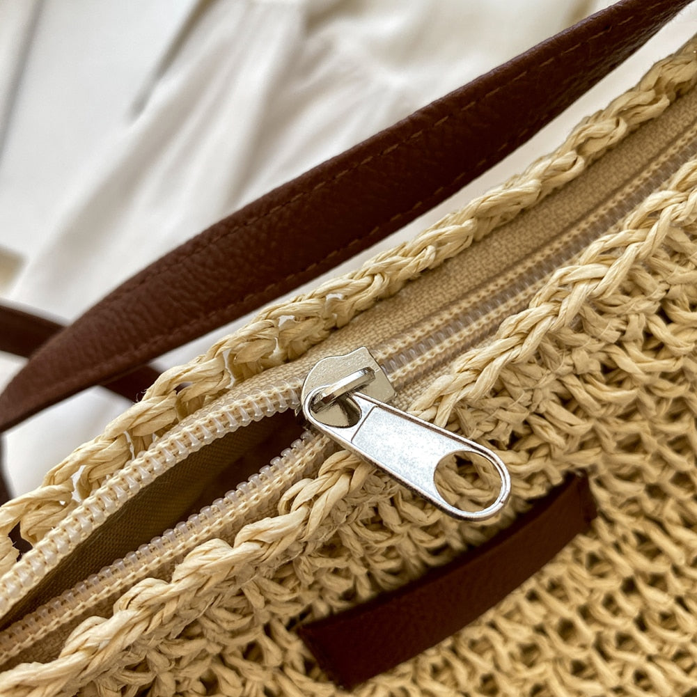Sac en paille tressée avec fermeture éclair argentée et anses en cuir marron, posé sur un fond blanc. Accessoire mode estival élégant.