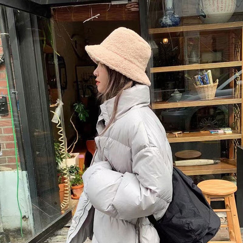 Femme portant un manteau doudoune gris et un chapeau en laine beige, marchant devant une vitrine de magasin. Mode hiver, style urbain.