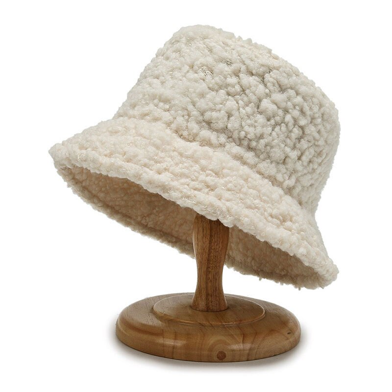 Chapeau bob en laine bouclée crème sur support en bois, accessoire mode hiver tendance, texture douce et chaude, style décontracté élégant.