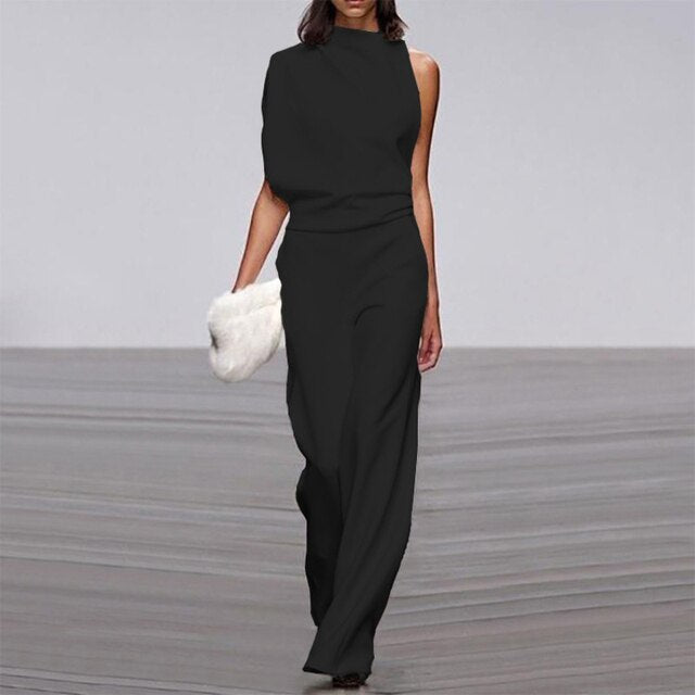Robe noire asymétrique élégante, sans manches, portée par un mannequin sur un podium, tenant une pochette blanche. Mode haute couture moderne.