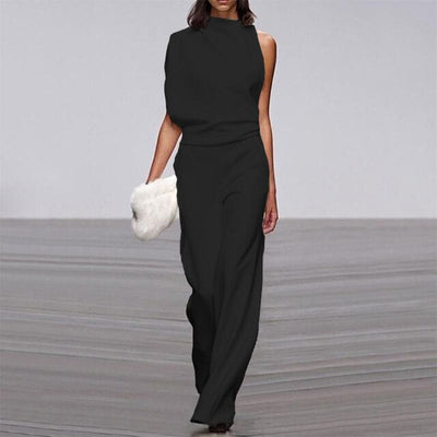 Robe noire asymétrique élégante, sans manches, portée par un mannequin sur un podium, tenant une pochette blanche. Mode haute couture moderne.