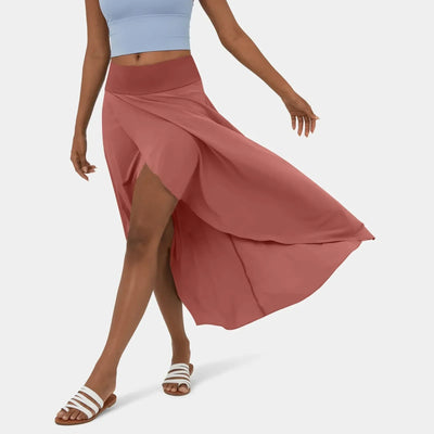 Femme portant une jupe longue rose fendue, associée à un haut bleu et des sandales blanches. Mode estivale élégante et décontractée.