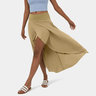 Femme portant une jupe longue beige fluide avec fente, associée à un haut bleu et des sandales blanches. Mode estivale élégante et décontractée.