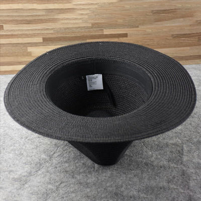 Chapeau noir en paille, intérieur visible avec étiquette, posé sur sol en bois et tapis gris. Accessoire de mode élégant et tendance.