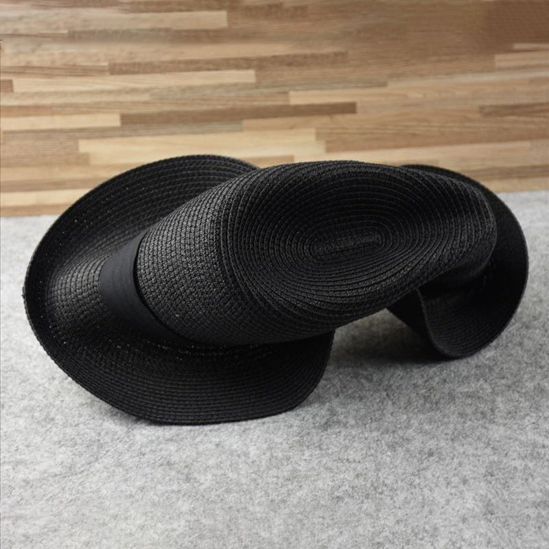 Chapeau noir en paille tressée, design sculptural, posé sur fond en bois et tapis gris. Accessoire de mode unique et élégant.