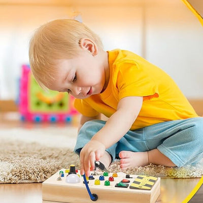 Enfant jouant avec un tableau d'activités en bois, boutons colorés et leviers, sur un tapis moelleux. Jouet éducatif, développement sensoriel.