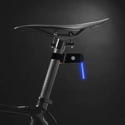 Selle de vélo en fibre de carbone avec feu arrière LED bleu, fixée sur une tige de selle, sur fond noir. Accessoire de sécurité cycliste moderne.
