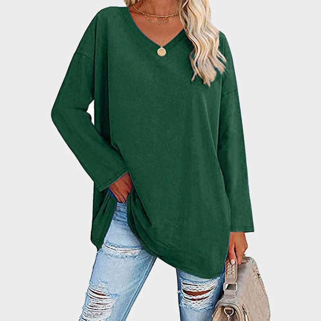 Femme portant un pull vert ample à col en V, associé à un jean déchiré et un sac beige. Mode décontractée, tendance automne-hiver.