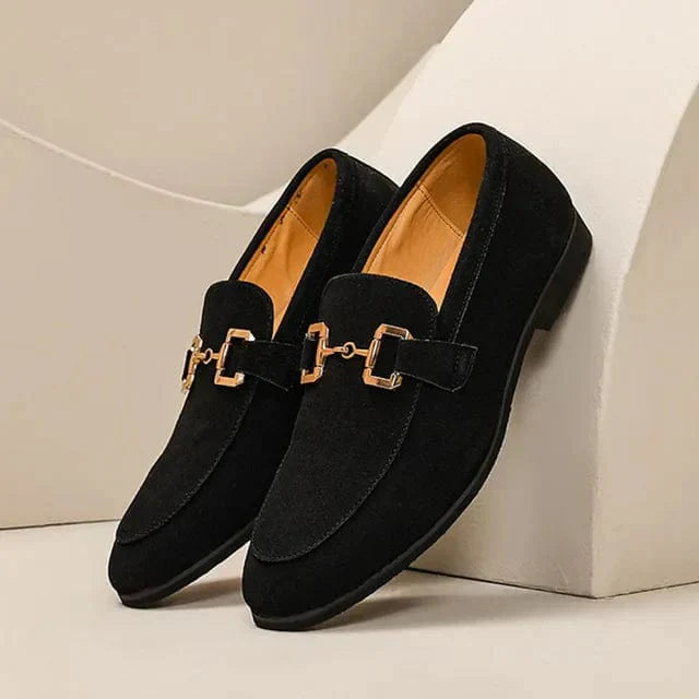 Paire de mocassins noirs en daim pour homme avec boucle dorée, élégants et modernes, posés sur fond beige. Chaussures habillées tendance.