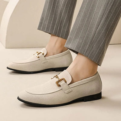 Chaussures mocassins beiges élégantes avec boucle dorée, portées avec un pantalon gris à rayures. Mode homme, style chic et moderne.