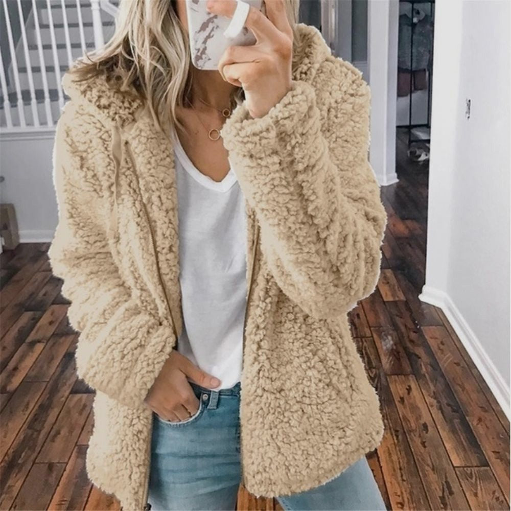 Femme portant un manteau en fausse fourrure beige, t-shirt blanc et jean, tenant un smartphone. Mode automne-hiver, style décontracté.