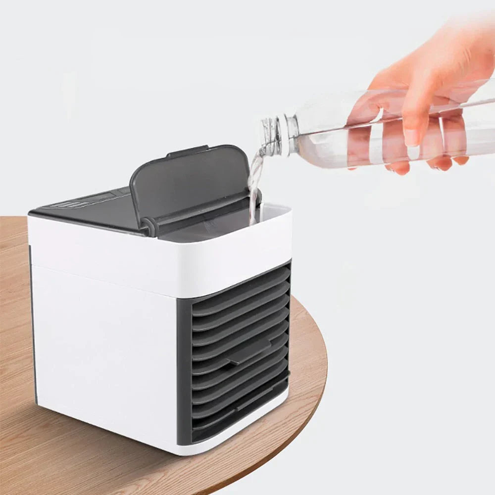 Petit climatiseur portable blanc sur une table en bois, avec une main versant de l'eau dans le réservoir. Refroidisseur d'air compact et efficace.