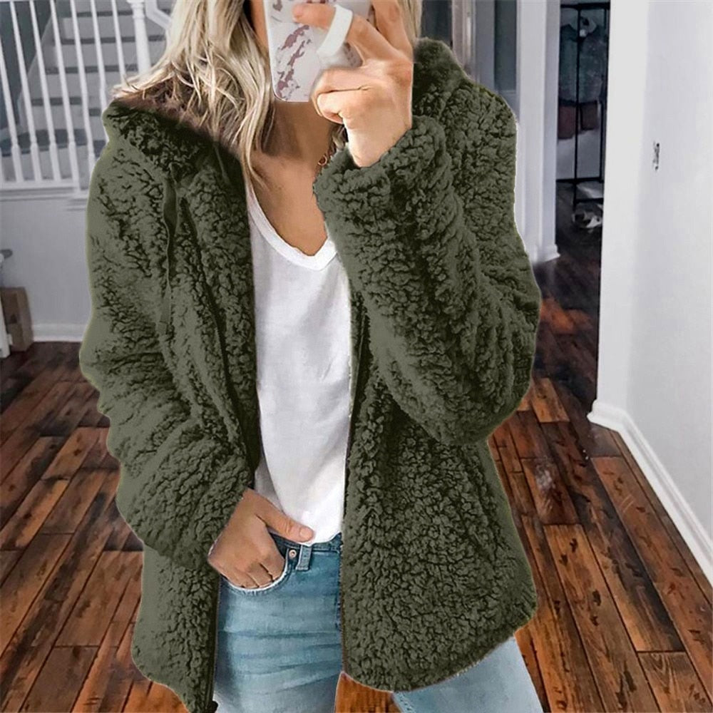 Femme portant une veste en fausse fourrure verte, style décontracté, sur un t-shirt blanc, debout sur un sol en bois. Mode automne-hiver tendance.