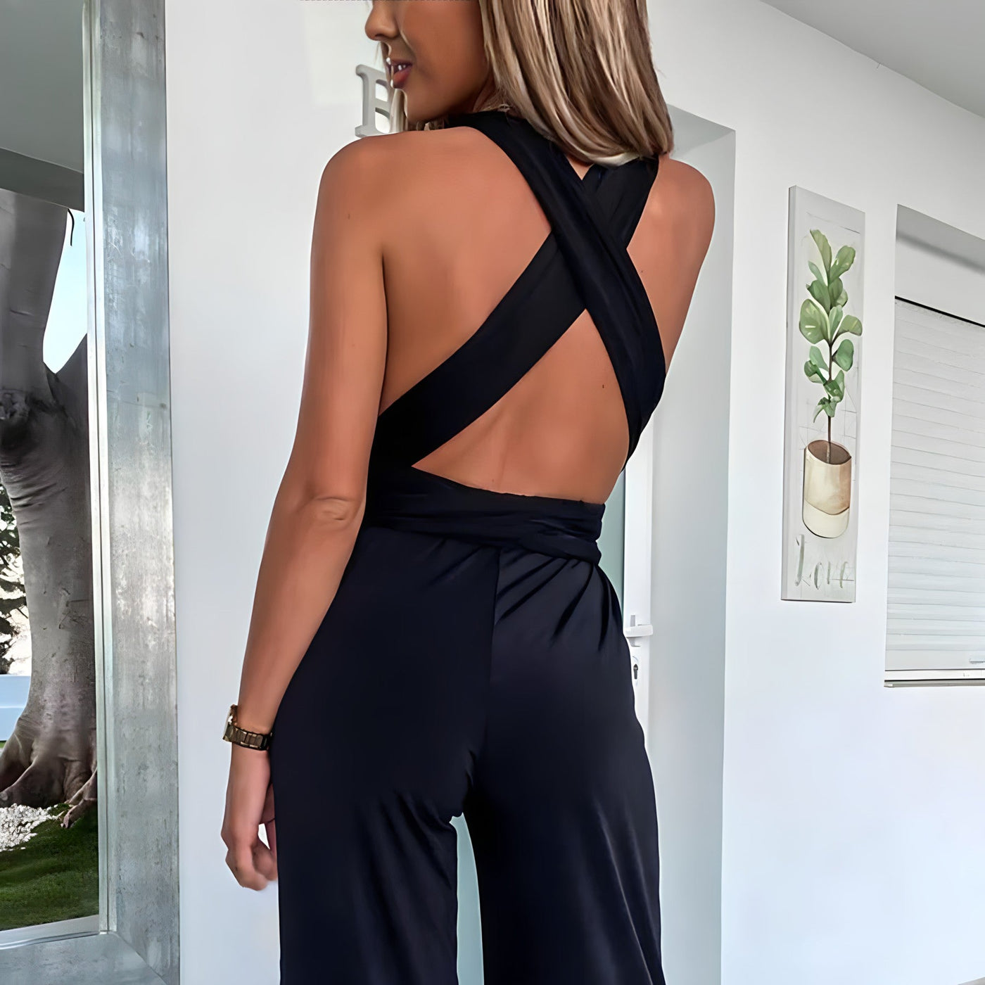Femme portant une combinaison noire dos nu croisé, debout dans un intérieur moderne. Mode élégante, tenue chic, style contemporain.