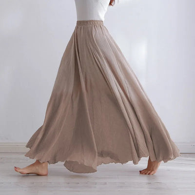 Femme portant une longue jupe beige fluide, marchant pieds nus sur un sol en bois clair. Mode élégante, style décontracté, tenue féminine.