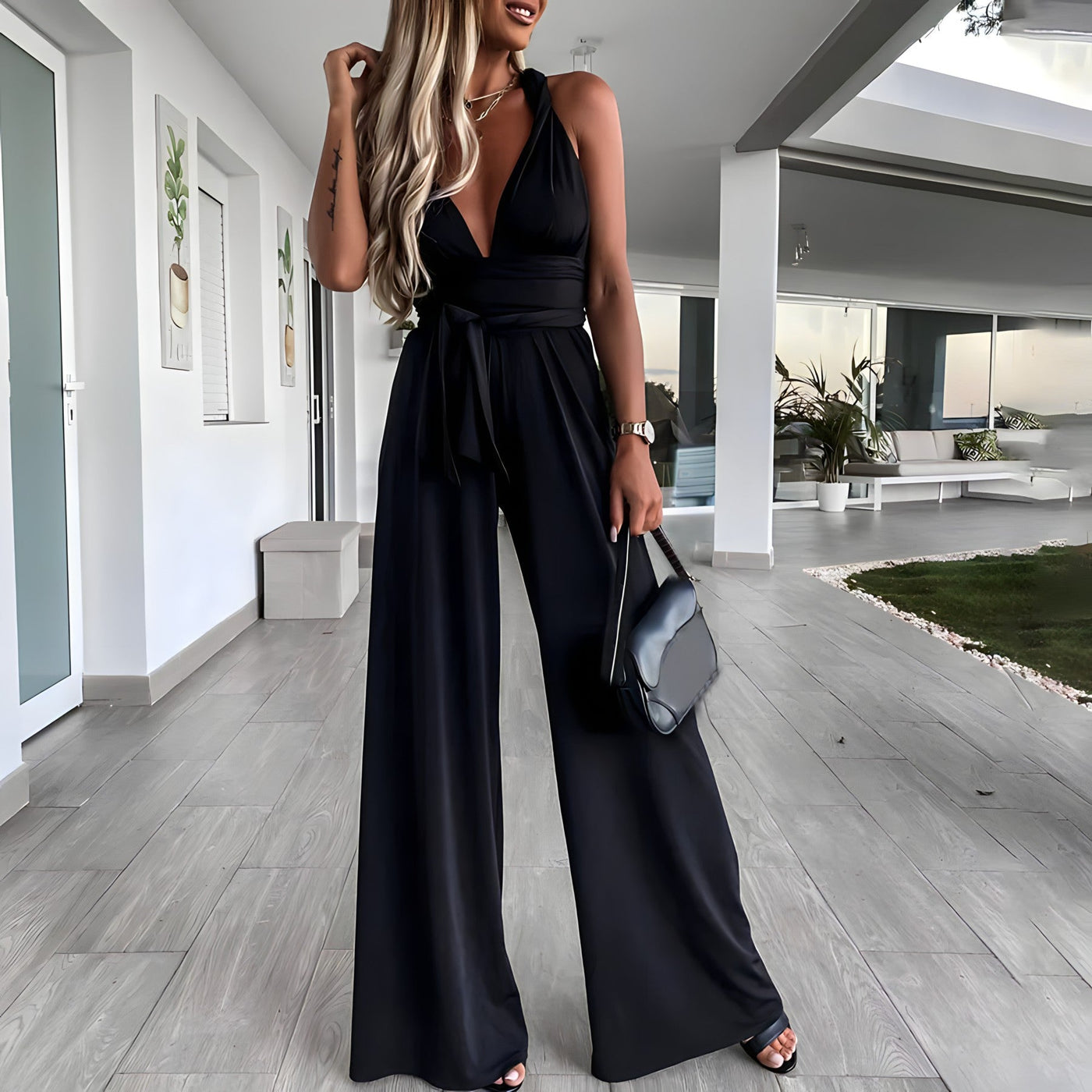 Femme en combinaison noire élégante, tenant un sac à main, dans un intérieur moderne. Mode chic, tenue de soirée, style glamour.
