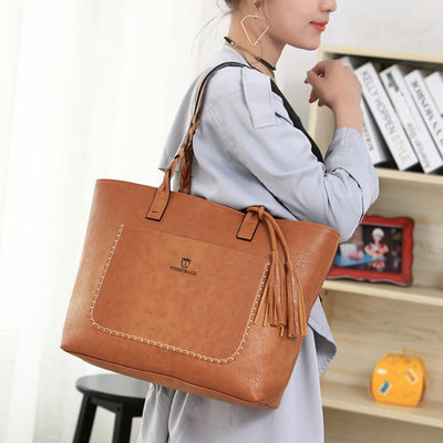Femme portant un grand sac à main en cuir marron avec franges, tenue décontractée, étagère en arrière-plan. Accessoire mode élégant et pratique.