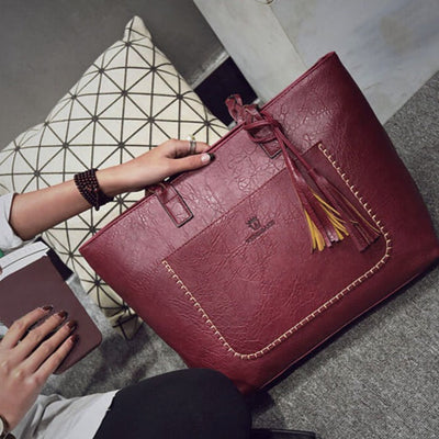 Sac à main en cuir rouge bordeaux avec coutures apparentes, pompons décoratifs, porté par une femme. Accessoire mode élégant et tendance.