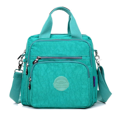 Sac à main turquoise en nylon avec bandoulière réglable, poches zippées multiples et logo. Accessoire mode femme, pratique et tendance.