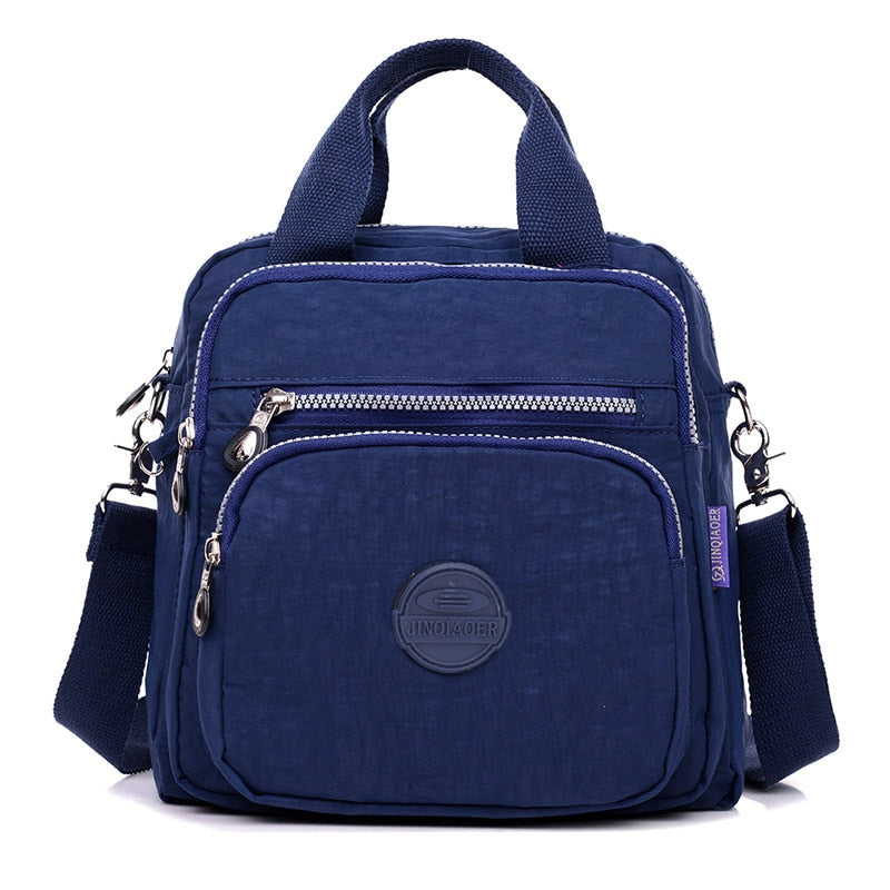 Sac à bandoulière bleu marine en toile, avec plusieurs poches zippées et une poignée supérieure. Design pratique et moderne pour un usage quotidien.