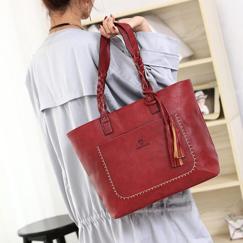 Sac à main en cuir rouge avec anses tressées, porté par une femme en robe grise. Design élégant, idéal pour la mode féminine et accessoires tendance.