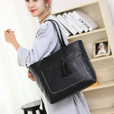 Femme portant un grand sac à main noir en cuir avec franges, devant une étagère. Mode féminine, accessoire tendance, style élégant.