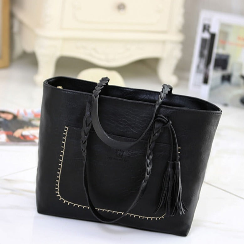 Sac à main noir en cuir avec coutures décoratives et pompon, posé sur un sol en marbre blanc. Accessoire mode élégant et tendance.