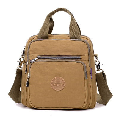 Sac à main en toile beige avec bandoulière réglable, poches zippées et logo circulaire. Style décontracté, idéal pour le quotidien et les voyages.