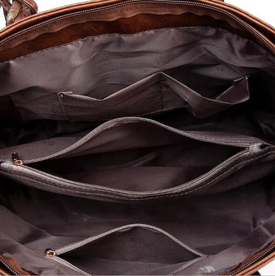 Intérieur d'un sac à main en cuir marron avec plusieurs compartiments et poches zippées, doublure en tissu gris. Accessoire mode femme élégant.