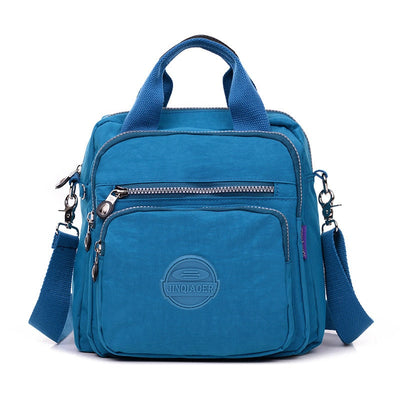 Sac à main bleu en nylon avec bandoulière réglable, poches zippées et logo. Idéal pour femme, mode, pratique, léger et résistant.