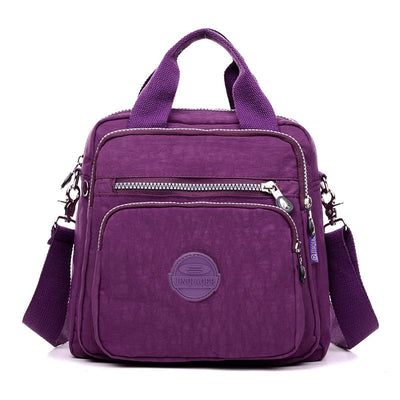 Sac à main violet en nylon avec bandoulière réglable, poches zippées, design moderne. Accessoire mode femme, pratique et élégant.
