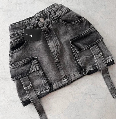 Jupe en jean noir délavé avec poches cargo et ceinture, posée sur fond gris. Mode urbaine, tendance streetwear, style décontracté.