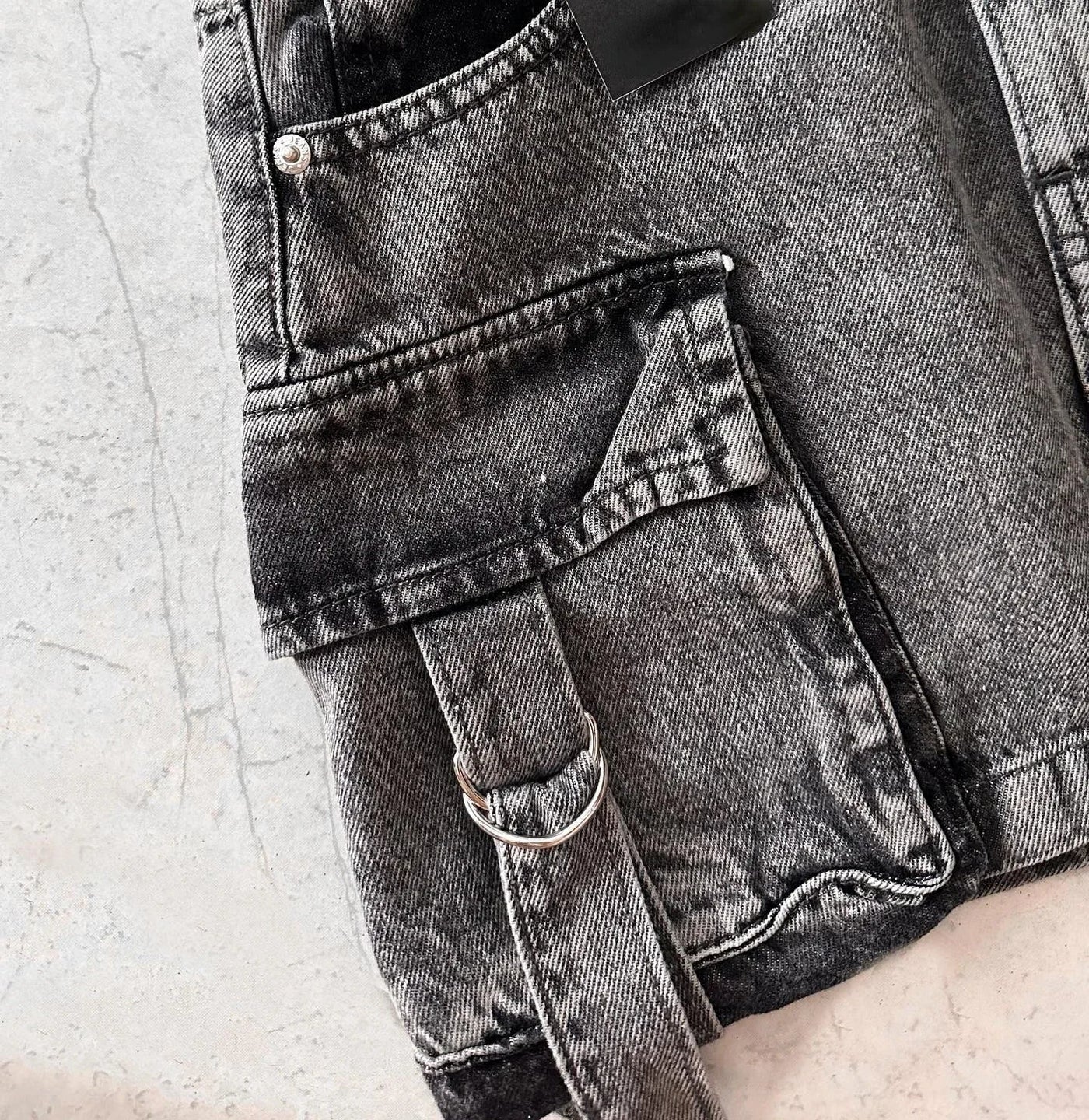 Jeans gris délavé avec poche avant et boucle métallique, style décontracté. Tissu denim texturé, tendance mode urbaine.
