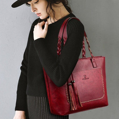 Femme portant un sac à main rouge en cuir avec franges, tenue noire élégante, mode automne, accessoires tendance, style chic et moderne.