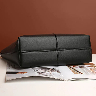 Sac à main noir en cuir synthétique sur une table, avec magazine ouvert en arrière-plan. Accessoire mode élégant, design moderne.