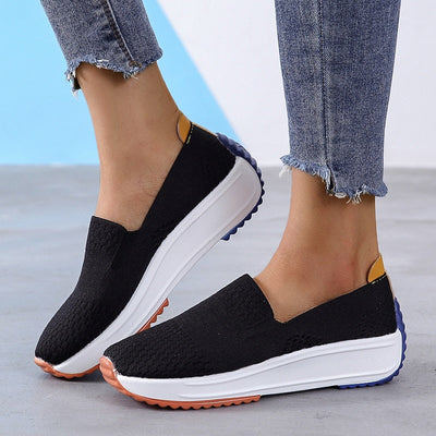 Chaussures de sport noires pour femmes avec semelles blanches, portées avec un jean. Confortables et tendance, idéales pour la marche.