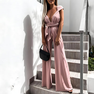 Femme en combinaison rose élégante, tenant un sac à main noir, posant sur des escaliers modernes. Mode féminine, tenue chic, style urbain.
