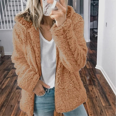 Femme portant un manteau en fausse fourrure beige, t-shirt blanc et jean, tenant un smartphone. Mode automne-hiver, style décontracté.