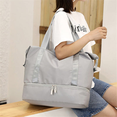 Sac à main gris en tissu imperméable, porté par une femme en t-shirt blanc et short en jean. Idéal pour le voyage et le quotidien.