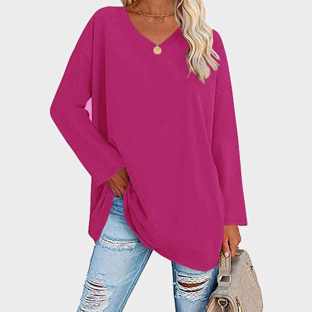 Femme portant un pull rose ample à col en V, associé à un jean déchiré et un sac beige. Mode décontractée, tendance automne-hiver.
