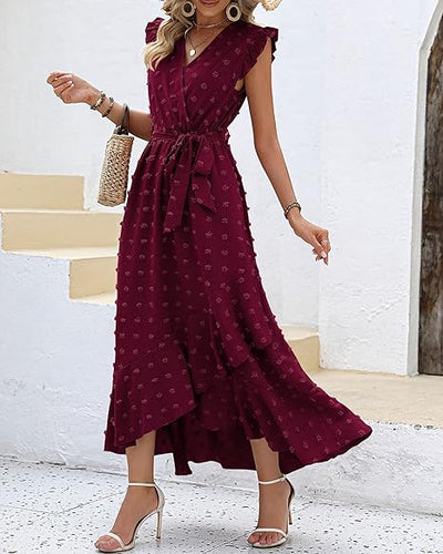 Robe longue bordeaux à volants, sans manches, ceinturée à la taille, portée avec des sandales à talons et un sac en osier. Mode féminine élégante.