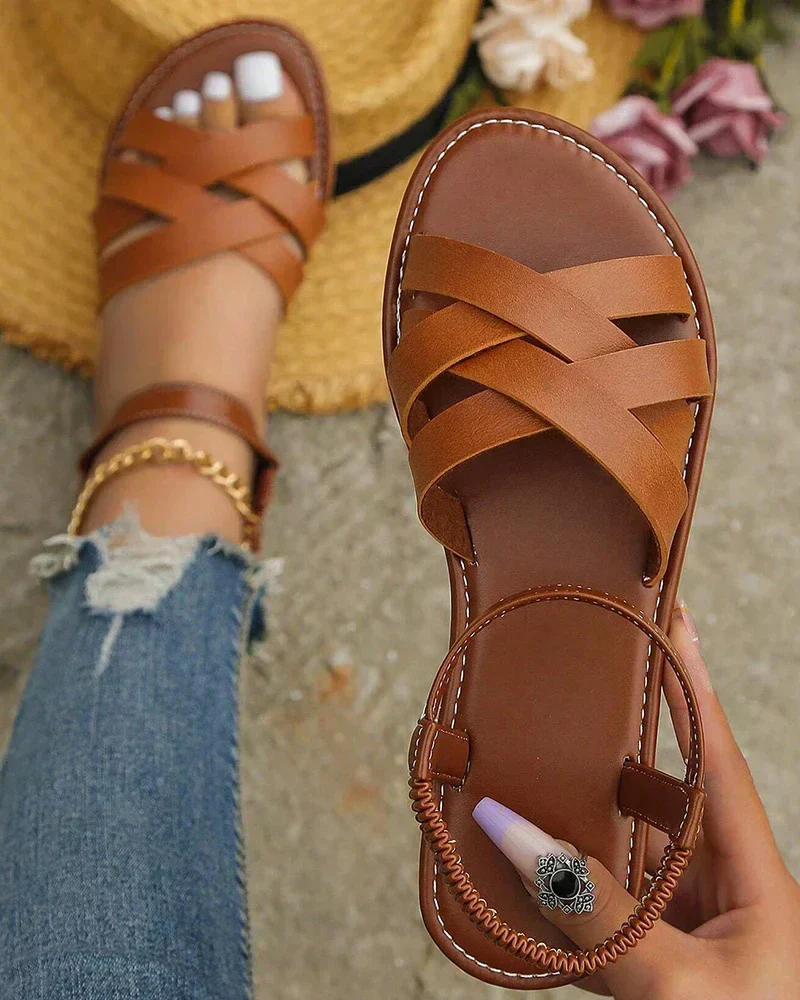 Sandales en cuir marron croisées pour femme, portées avec un jean déchiré et un chapeau de paille. Mode estivale, chaussures confortables.